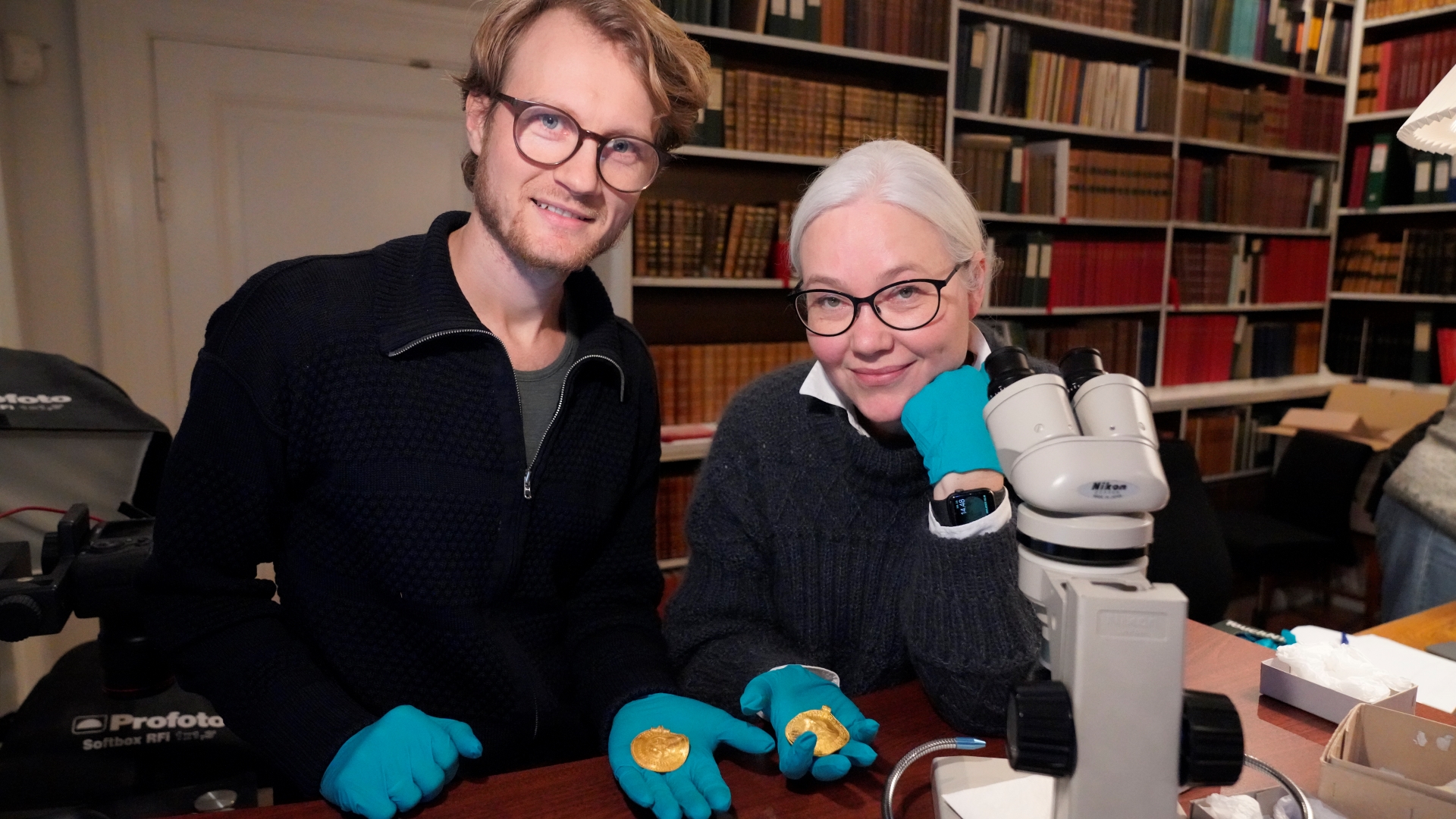 Opdagelsen er gjort af forskerne Krister Vasshus og Lisbeth Imer, der her står med to brakteater fra Vindelevskatten. Den i Lisbeths hånd har indskriften "Han er Odins mand". Foto: John Fhær Engedal Nissen, Nationalmuseet.