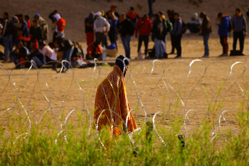 Migrants stand near the border wall, as seen from Ciudad Juarez