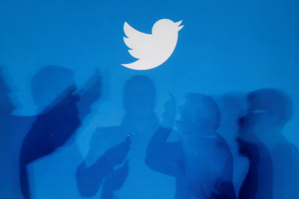 FILE PHOTO: Shadows of people holding mobile phones are cast onto a backdrop projected with the Twitter logo in Warsaw