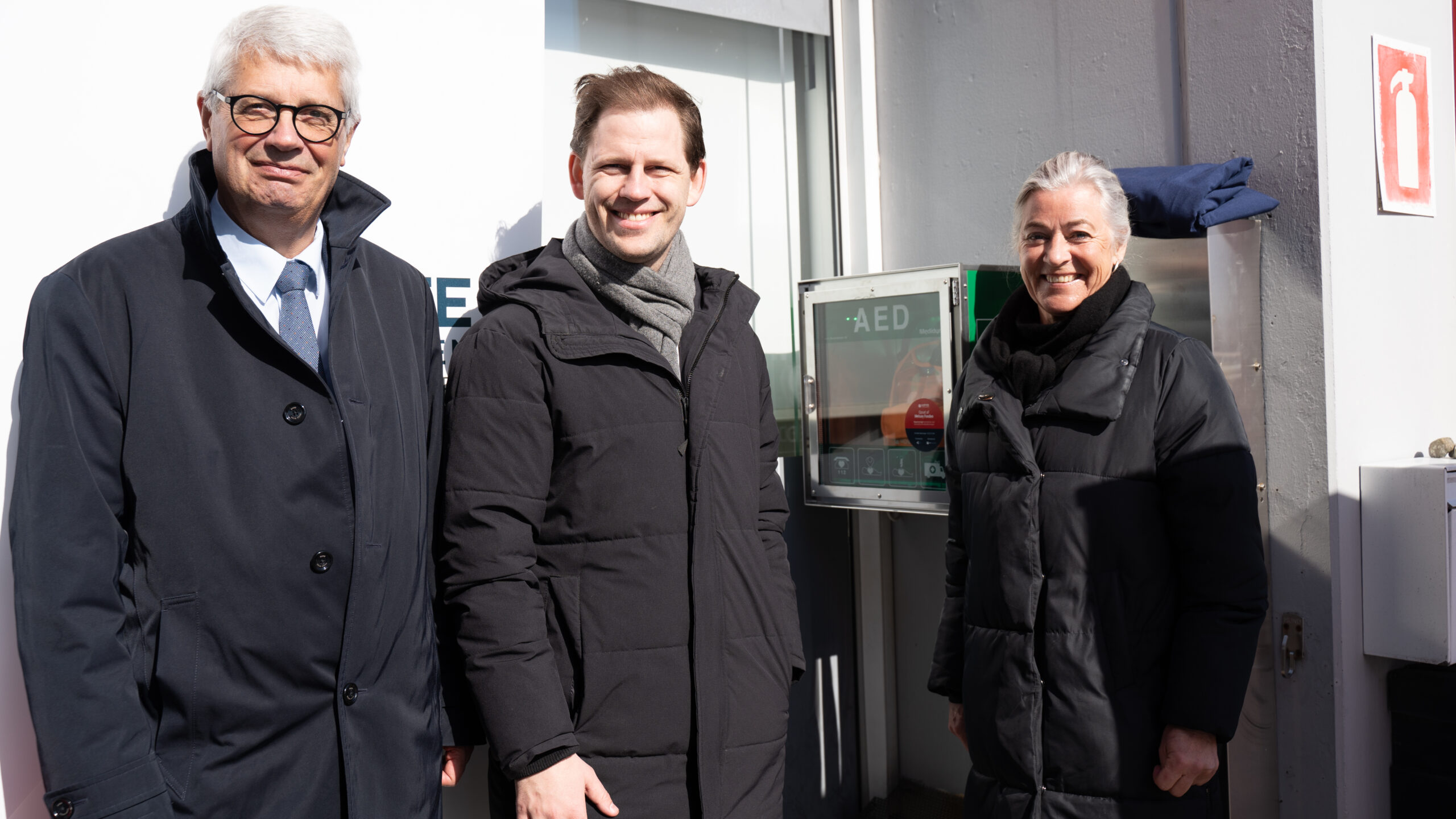 Anker Laden-Andersen, formand, Melsen Fonden, Mads Duedahl, Regionsrådsformand (V), Region Nordjylland, Anne Kaltoft, adm. direktør, Hjerteforeningen, foran den nye hjertestarter. Foto: Hjerteforeningen