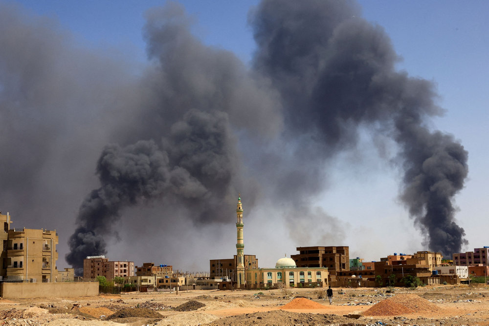 Man walks while smoke rises above buildings after aerial bombardment in Khartoum North