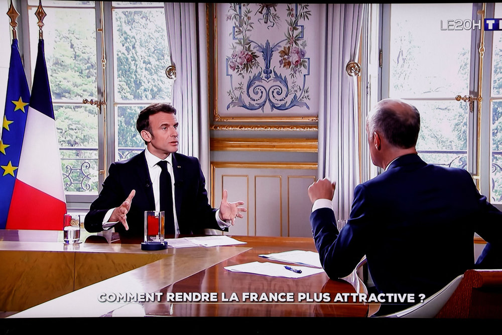 French President Macron is seen om a screen as he attends an interview in Paris