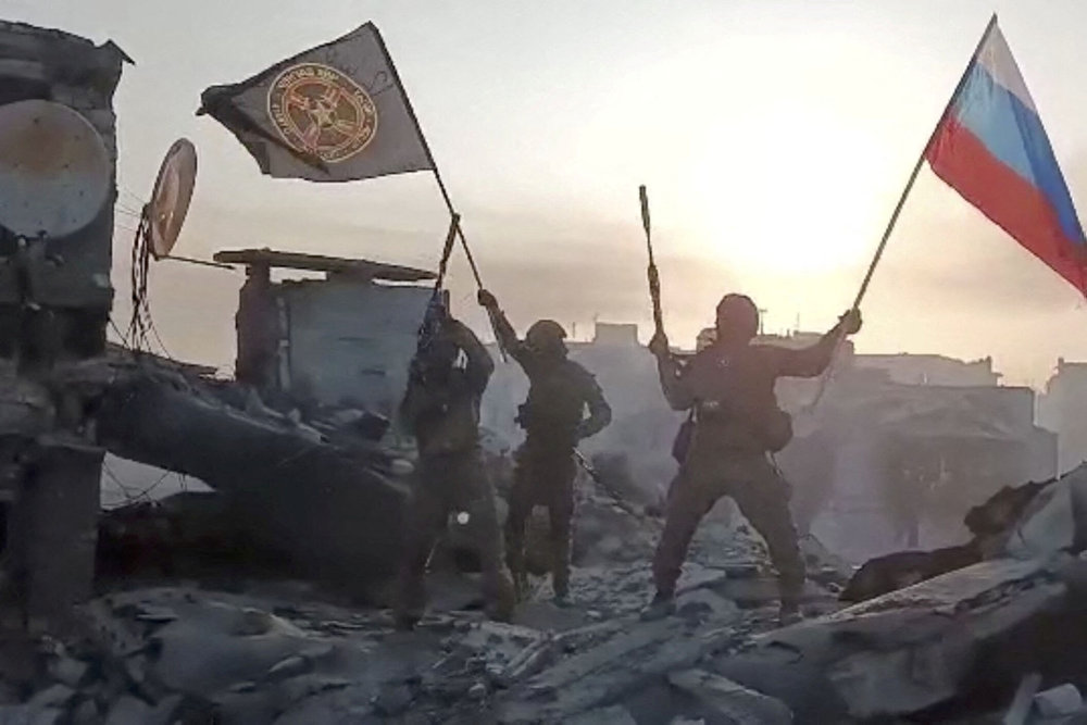 Wagner mercenary group fighters wave flags on top of a building in an unidentified location