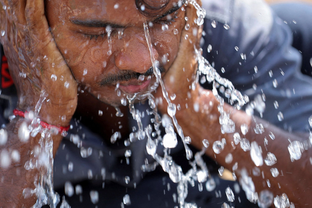 A labourer washes his face with water leaking from a roadside pipe on a hot summer day in New Delhi
