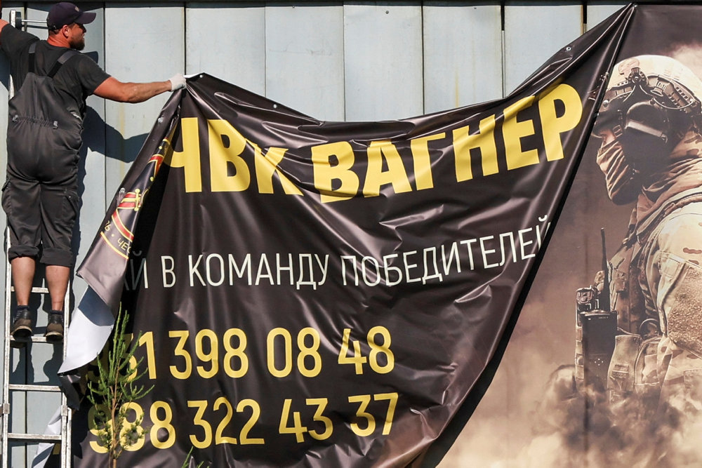 A worker remotes a banner promoting service in Wagner group in Saint Petersburg