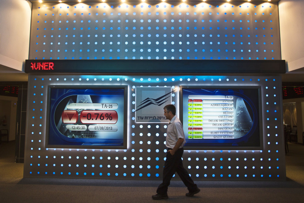 Employee walks past screen displaying market data at the Tel Aviv Stock Exchange